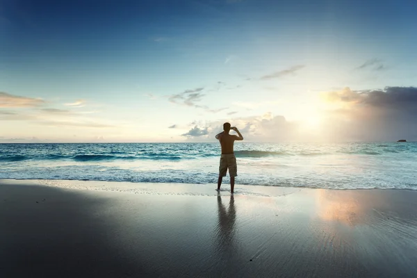 年轻的男子在海滩上的移动电话上拍张照片 — 图库照片