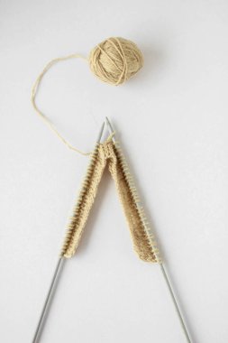 Üst görünüm bej iplik ve örgü iğneleri beyaz arka planda izole edilmiş.