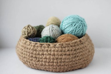 Beyaz bir arka planda, yeşil bir sepetin içindeki renkli iplik derileri...