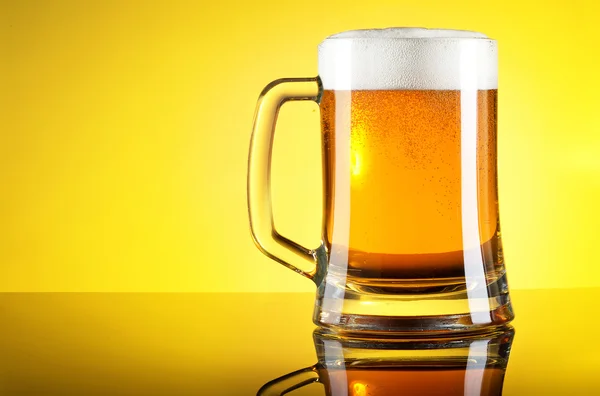 Glass of beer close-up with froth over yellow background — Stock Photo, Image