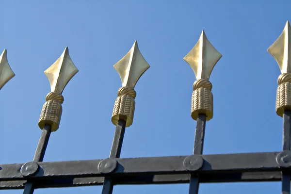 Золотые шипы на железном заборе над голубым небом — стоковое фото