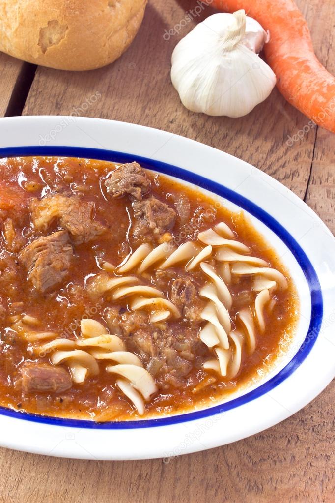 Beef goulash with pasta on wooden background
