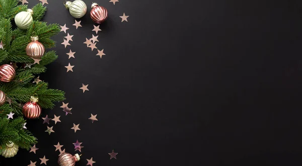 Vánoční a novoroční kompozice. Zdobené růžové koule, smrková větev leží na černém pozadí s konfety v podobě hvězd. Byt ležel, horní pohled, kopírovací prostor — Stock fotografie