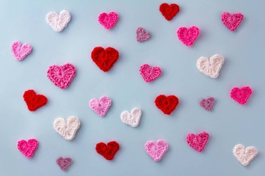 Mavi arka planda pembe, beyaz ve kırmızı kalpler örülmüş. Sevgililer Günü konsepti. Tığ işi. Üst görünüm