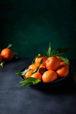 Koyu arkaplanda yeşil yapraklı taze mandalinalar, seçici odak resmi
