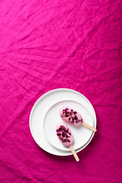 Ice cream bar with pink topping and flower petals on the fuchsia tablecloth, selective focus image