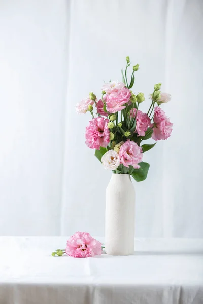 白いリネンのテーブルクロスの上に白い花瓶にピンクのリアンサスの花 選択的な焦点画像 — ストック写真