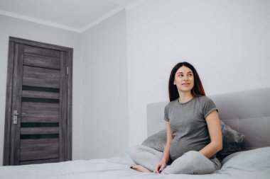 Genç preganant kadın yatakta kapalı rahatlatıcı bir bebek bekliyor