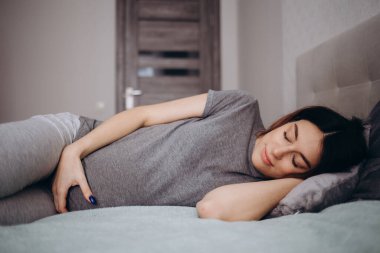 Güzel hamile bir kadın yatakta karın destek yastığıyla uyuyor ya da dinleniyor. Bebek bekleyen genç bir anne. Hamilelik kavramı, annelik, sağlık, jinekoloji, tıp.