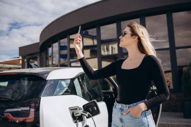 Elektrikli benzin istasyonunda kadın elektro arabayı şarj ediyor.