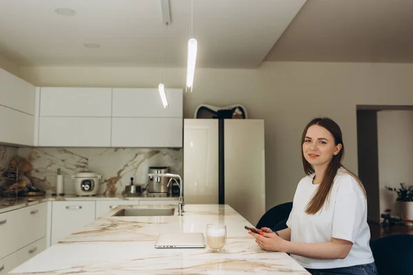 Jonge Vrouw Met Behulp Van Smartphone Leunend Keukentafel Met Koffiemok — Stockfoto