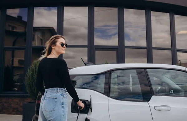 Jovem Mulher Está Perto Carro Elétrico Olha Para Telefone Inteligente — Fotografia de Stock