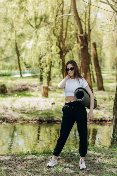 Yoga minderi yuvarlayan kadın. Sabah güneşinde hasırda egzersiz yapmak. Egzersizden önce kadın eller yoga minderini açıyor. Sağlıklı bir yaşam tarzı. Dersten sonra parkta yoga minderi tutan genç bir kadın..
