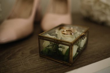 Beyaz masada duran güllerle dolu cam kutuda alyanslar. Düğün aksesuarları