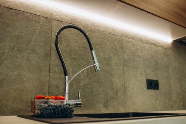 Siyah mutfak musluğu gümüş lavabonun üzerinde, su bardağının yanında.