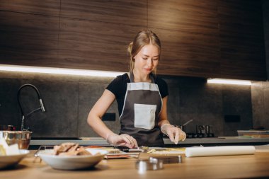 Güzel genç bir kadın modern bir mutfakta tatlı hamur işleri hazırlıyor.