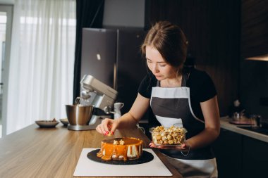 Tatlıcı çilek ile beyaz krem ve çikolata ile bir bisküvi kek dekorlar. Pasta beyaz bir masada ahşap bir stand üzerinde duruyor. Ev yapımı pasta kavramı, yemek pastaları.