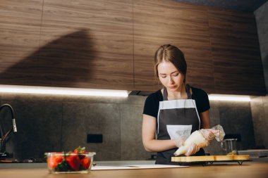 Dost gülümseyen kadın profesyonel pudra bir hamur işi çanta kullanarak kremalı çörek tepesi portresi. Kameraya bakıyor. Kapalı görüntü. Pasta şefi kadın kremalı kek yapma
