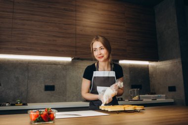 Güzel genç kadın pastacı modern mutfağın arka planında tatlılar hazırlıyor.