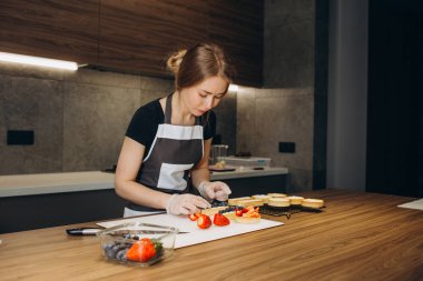 Kadınların elleri çikolatalı kekleri taze çilekle süslüyor. Meyveli kek pişirme işlemi