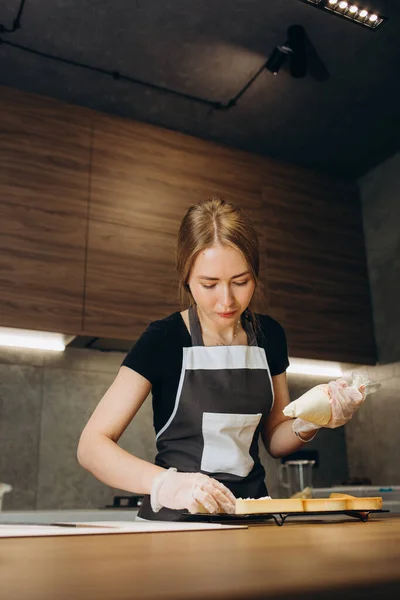 Beautiful young woman confectioner prepares sweets on a background of modern kitchen