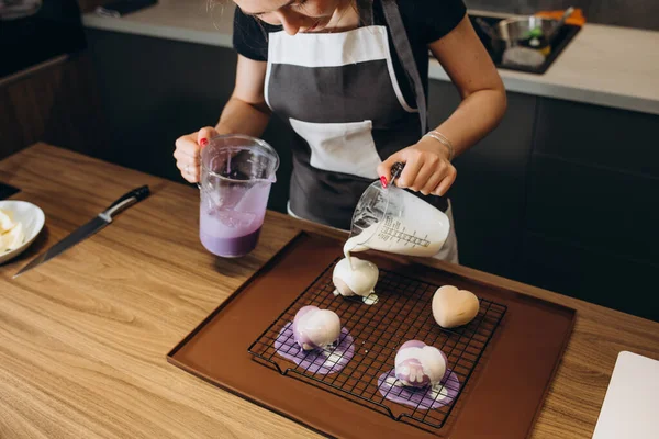 Young female pastry chef pours liquid mousse into a mold. Preparation of cake, dessert in a professional kitchen.
