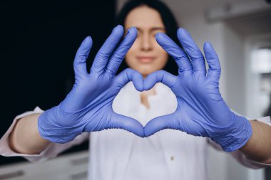 Hastaya sevgilerimle. Beyaz laboratuvar önlüklü genç kadın doktor kameranın karşısında birleşik parmakları kalbi yapıyor. Profesyonel kardiyolog insanlardan kardiyo sağlığıyla ilgilenmelerini istedi