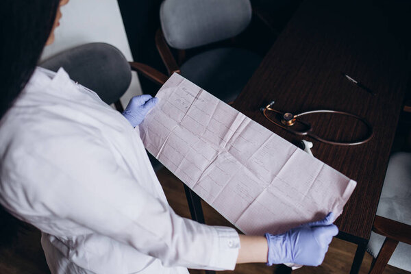 Кардиограмма сердца в руках врача крупным планом. Кардиолог изучает показания электрокардиографа.