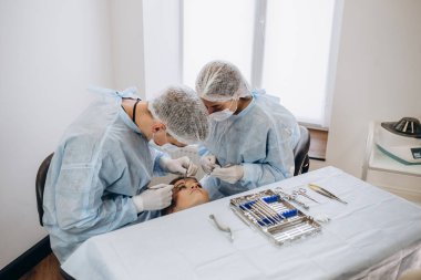 Üniformalı bir cerrah ekibi, estetik cerrahi kliniğindeki bir hastayı ameliyat ediyor.