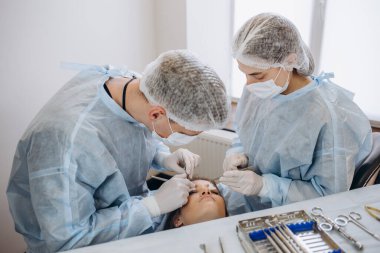 Konsantre cerrahi ekibi ameliyathanede bir hastayı ameliyat ediyor. Karmaşık makinelerle yıllarca eğitim almış iyi eğitimli bir anestezi uzmanı ameliyat boyunca hastayı takip eder..