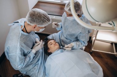 Doktorun el penslerini tamponla tutarken cerrah ve asistanın arka planda estetik ameliyat yapmasını kapat. Ameliyathanede çeşitli cerrahi aletler kullanan tıbbi ekip..