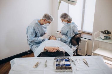 Doktorun el penslerini tamponla tutarken cerrah ve asistanın arka planda estetik ameliyat yapmasını kapat. Ameliyathanede çeşitli cerrahi aletler kullanan tıbbi ekip..