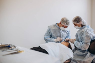 Üniformalı bir cerrah ekibi, estetik cerrahi kliniğindeki bir hastayı ameliyat ediyor.