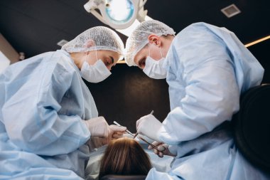 Modern ameliyathanede cerrahi operasyon yapan profesyonel tıbbi ekip. Asyalı asistan, hastanedeki yoğun bakım hastasının ameliyat sırasında cerrahlara aletler dağıttı..