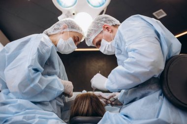 Üniformalı bir cerrah ekibi, estetik cerrahi kliniğindeki bir hastayı ameliyat ediyor.