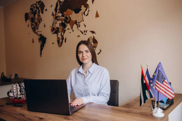 Young travel agent successful secretary employee business woman in casual shirt sit work at white office desk with pc laptop hold Earth world globe isolated on pastel blue background studio portrait.