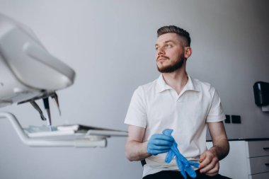 Beyaz üniformalı genç bir dişçinin portresi modern ekipmanlarla bir dişçide bir sandalyede oturuyor..