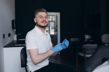 Erkek dişçi hastalarıyla çalışmak için eldivenlerini takıyor.