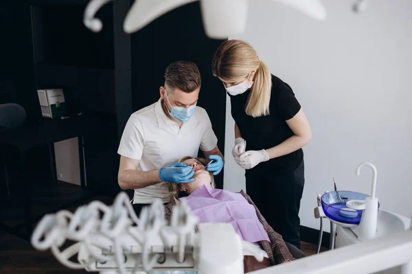 Modern stomatology private clinic with professional equipment. Dentists working with client\'s teeth. Woman lying on dentist cahir. Doctors wearing in medical caps, unforms and masks.