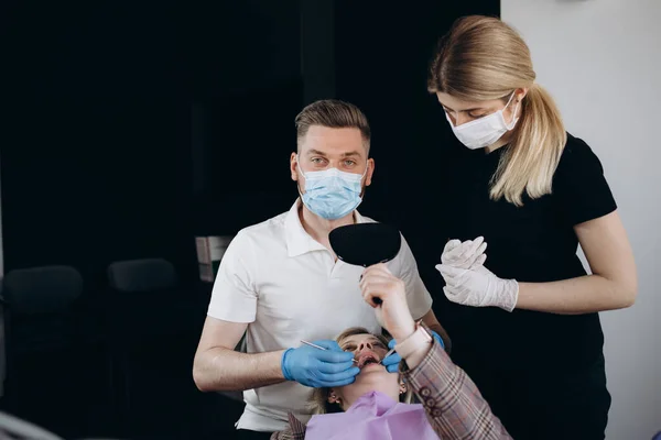 Modern stomatology private clinic with professional equipment. Dentists working with client\'s teeth. Woman lying on dentist cahir. Doctors wearing in medical caps, unforms and masks.