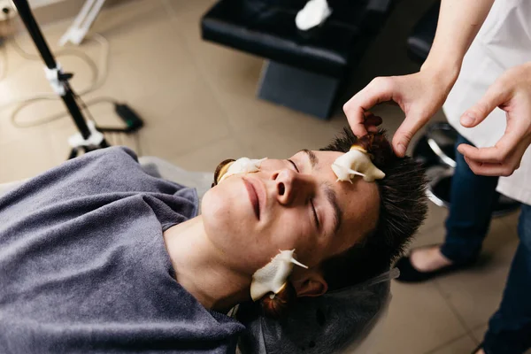 Beyaz bir genç, salyangoz masajı yaptırıyor. Cilt terapisi ve salyangozlarla kaplıca salonunda bakım. Cilt yenilenmesinin modern kozmetolojik prosedürü.