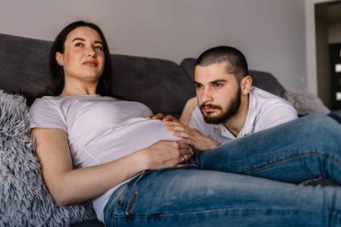 portre Bebek Patiği tutan mutlu bir hamile kadın ve kocası evde kanepe üzerinde