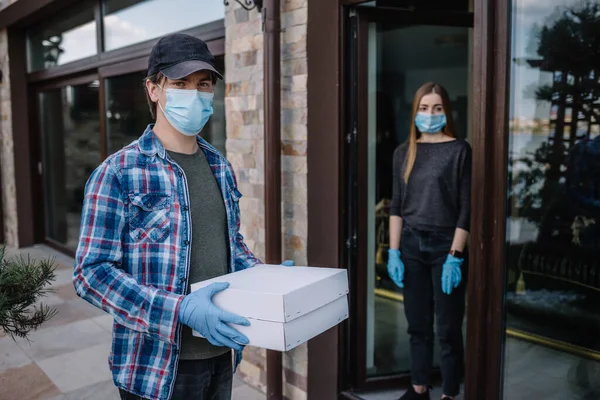 Courier and protective mask delivers parcels, customer and medical gloves receives box. Delivery service under quarantine, disease outbreak, coronavirus covid-19 pandemic conditions.