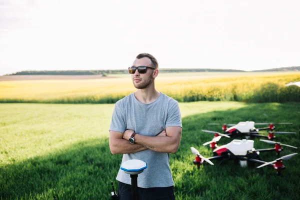 Küçük dron elinde uzaktan kumandayla çiftçinin önünde uçuyor. Dörtlü helikopter pilotun yanında uçuyor. Agronomist buğday tarlasında hava fotoğrafları ve videolar çekiyor. Tarım alanındaki yenilikler