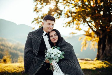 Düğün çifti dağların yakınında battaniyenin altında.