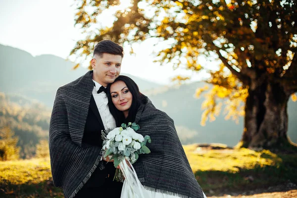 Düğün çifti dağların yakınında battaniyenin altında.