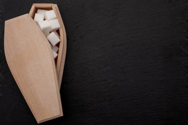 Diyabet hastalığı, insülin direnci ve ilave şekerler koyu siyah arka planda izole edilmiş şeker küpleriyle dolu tabut kavramınızı öldürüyor.