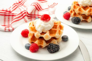 Sağlıklı kahvaltı, sağlıklı tatlı ve waffle konsepti temalı yaban mersinli, böğürtlenli, ahudutlu ve kırsal beyaz ahşap masada çırpılmış kremalı Belçika waffle 'ı.