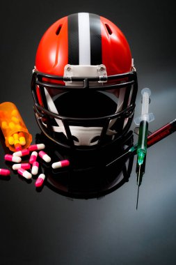 Performans artırıcı uyuşturucu kullanımı ve futbol kaskı ile doping konsepti, dökülen kapsül hapları ve kırmızı ve yeşil kimyasallı iki şırınga