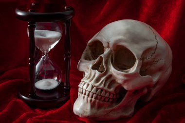 Yaşam coşkusu, ölüm korkusu ve kırmızı kadife arka planda kafatası ve eski bir kum saati ile Memento Mori konsepti.